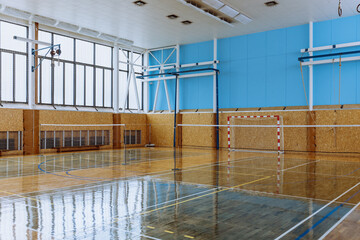 Empty indoor sports hall with shiny wooden floor, high ceilings, and goal post in the background