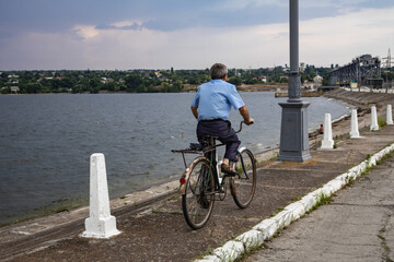 A man in a blue shirt rides a bicycle on the river bank