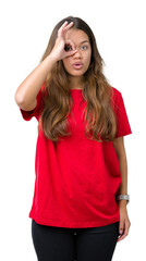 Fototapeta premium Young beautiful brunette woman wearing red t-shirt over isolated background doing ok gesture shocked with surprised face, eye looking through fingers. Unbelieving expression.