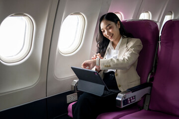 A woman is sitting on an airplane, wearing a white shirt and a tan jacket