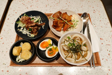 Japanese set meal with 5 different dishes including soup udon, boiled seasoned egg, stir fried pork, fried chicken and deep fried egg tofu with chopsticks and spoon