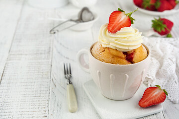 Strawberry banana mug cake. Fresh homemade cake in mug with strawberry, banana and whipped cream in white rustic ceramic mug cup on white wooden table background. Healthy breakfast cooked in microwave
