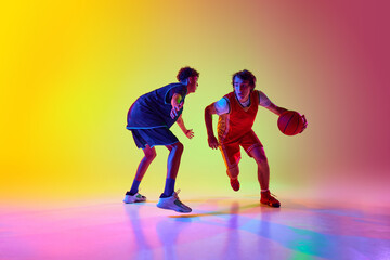Two basketball players train under vivid lights, demonstrating focus and skill in neon light against gradient studio background. Concept of professional sport, competition, match, team games. Ad