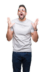Naklejka premium Young handsome man wearing sunglasses over isolated background crazy and mad shouting and yelling with aggressive expression and arms raised. Frustration concept.