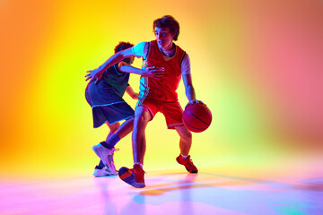 Intense basketball practice with two athletes in neon light against gradient studio background....