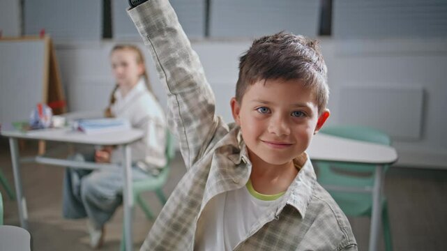 Portrait smart pupil studying at elementary school. Positive boy raising hand