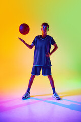 Young basketball player in sport blue uniform confidently poses with ball in neon light against...