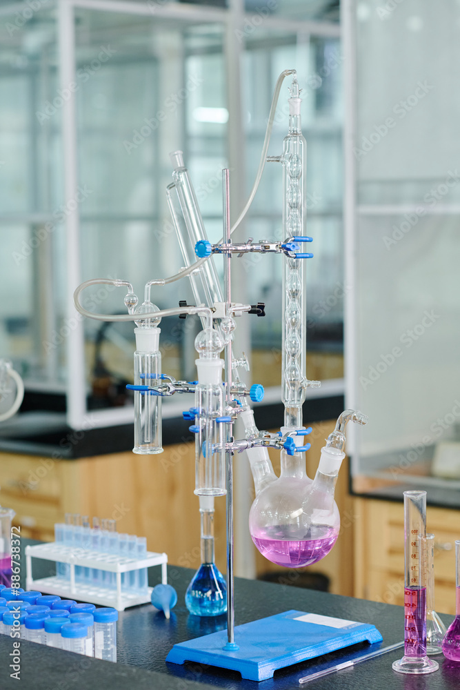 Poster stand with various glassware containing liquid substances on workplace of chemist or biotechnologist