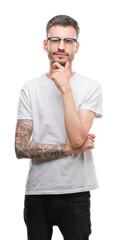 Young tattooed adult man looking confident at the camera with smile with crossed arms and hand raised on chin. Thinking positive.