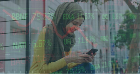 Image of graph, trading board, biracial woman wearing hijab smiling while chatting on cellphone