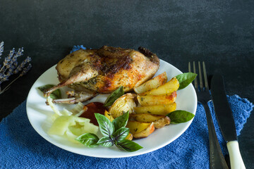 baked quail with potatoes and vegetables on plate on dark background
