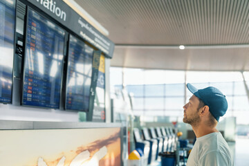 Man tourist in airport terminal checking flight information on digital board, preparing for check-in on his flight. Male traveler in airport terminal looks at airplane schedule board