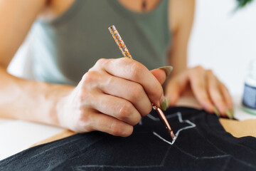 young woman draws picture on clothes with paints, handmade craft work. Customization