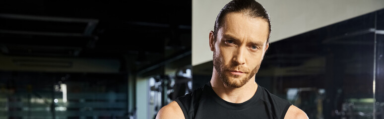 Obraz premium A man in active wear stands in front of a mirror at the gym, examining his form and muscles after a workout.