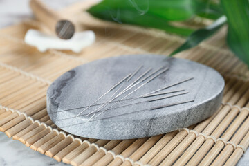 Grey stone coaster with acupuncture needles on bamboo mat, closeup