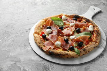 Tasty pizza with cured ham, olives, mozzarella cheese, sun-dried tomato and basil on gray textured table