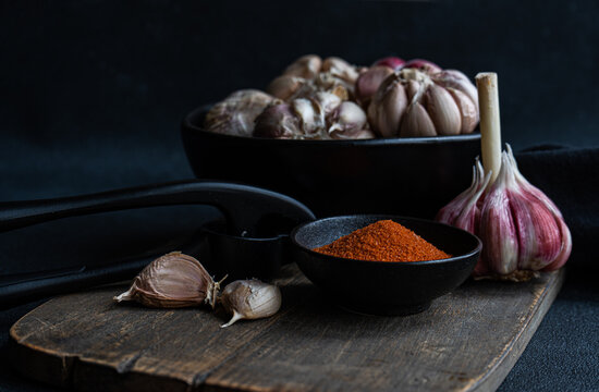 Close-up of a bowl of fresh garlic bulbs on a  chopping board with garlic cloves, chilli pepper salt and a garlic press
