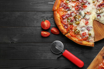 Delicious pizza Diablo, tomatoes and cutter on black wooden table, flat lay. Space for text