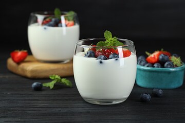 Tasty yogurt with fresh berries and mint in glasses on black wooden table, closeup