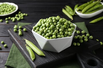 Fresh green peas in bowl and pods on black wooden table