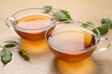 Refreshing green tea in cups and leaves on wooden table, closeup