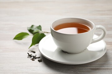 Refreshing green tea in cup and leaves on grey wooden table, closeup