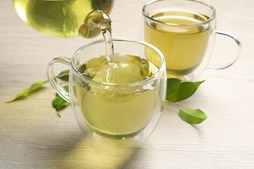 Pouring refreshing green tea into cup at wooden table, closeup