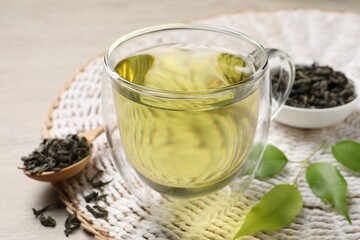 Refreshing green tea in cup, spoon and leaves on wooden table, closeup
