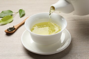 Pouring refreshing green tea into cup at wooden table, closeup