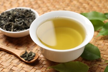 Refreshing green tea in cup, spoon and leaves on table, closeup