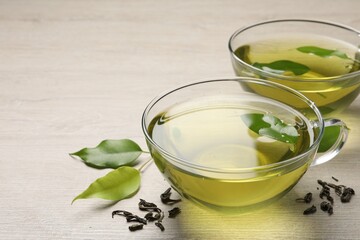 Refreshing green tea in cups and leaves on wooden table, closeup. Space for text