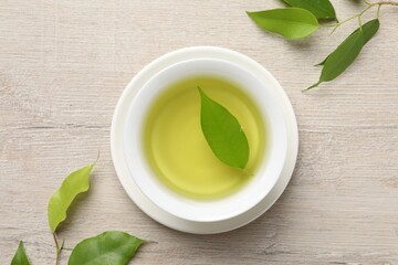Refreshing green tea in cup and leaves on wooden table, flat lay