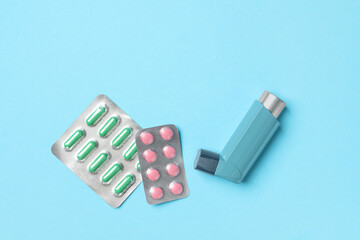 Asthma inhaler and pills on light blue background, flat lay