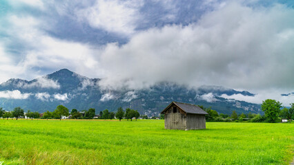 After a thunderstorm, scenery with barn and cabin on green field and sun rays through cloud, light and dark green grass after a long storm, white clouds under dark Thunderstorm