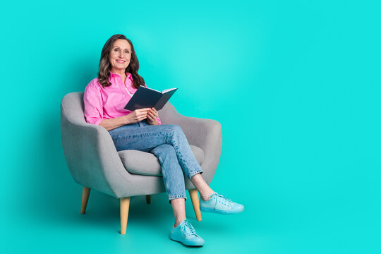 Full length photo of adorable lovely woman wear pink shirt sitting armchair enjoying book empty space isolated blue color background