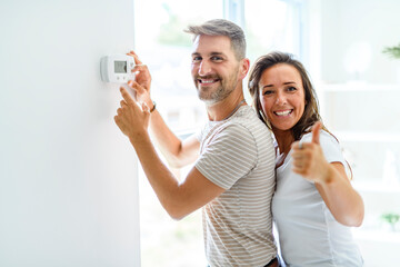 Smiling couple Adjusting Thermostat On Home Heating System