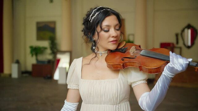 Beautiful woman professional musician plays a wooden on the violin. Pretty face girl violinist musician plays at event ball. lady in white vintage dress. creative hairstyle dark hair old style art 4k