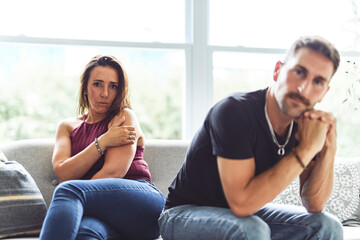 Unhappy, upset or sad with a couple arguing on a sofa in their home living room about an affair or breakup.