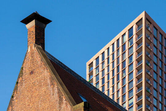 An architectural photograph featuring a historic brick chimney set against the clear sky, juxtaposed with a modern high-rise building in the backdrop symbolizing contrast  in Rotterdam