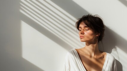 Naklejka premium A serene woman stands in sunlight with shadows falling across her face and background, capturing a moment of peace and reflection, enhanced by the play of light and shadow.