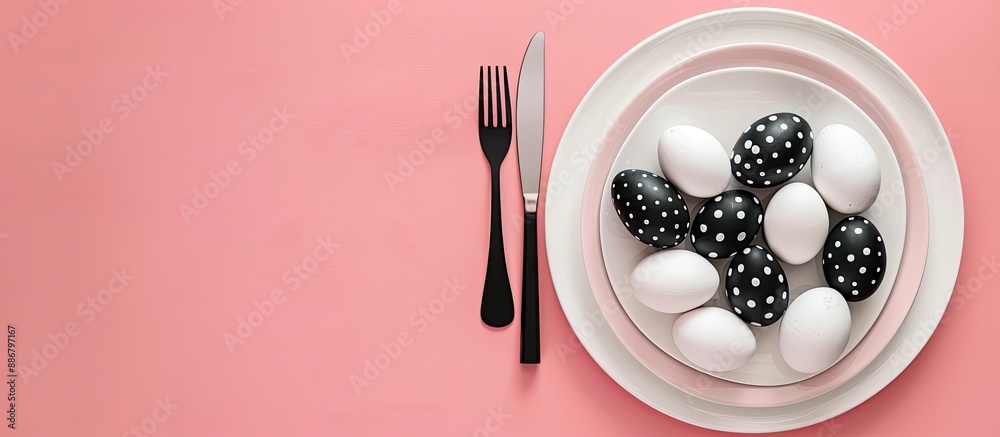 Poster top view of easter dinner setting featuring black and white eggs, knife, and fork on a pastel pink b