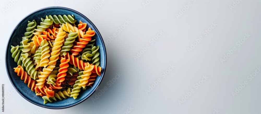 Poster ample copy space surrounds a vibrant array of spiral pasta in a blue bowl placed on a white surface.