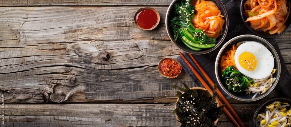 Poster aerial view of korean side dishes in bowls beside chopsticks and gimbap on a wooden table with copy 
