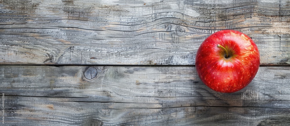 Poster A vibrant red apple resting on a rustic brown frame atop a gray wooden surface in a top-down view with copy space image included.