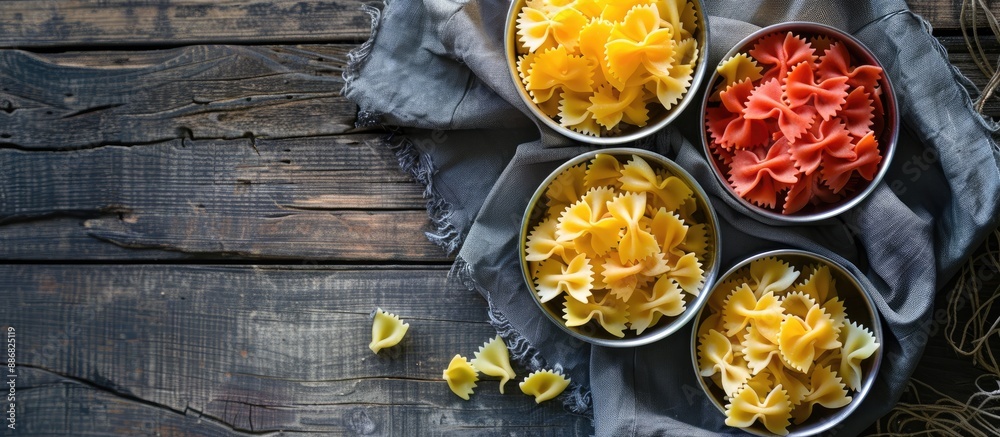 Poster Three colors of macaroni farfalle resting in a saucepan, on a napkin, and a wooden background, creating an appealing culinary composition with copy space image.