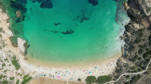 A bird's-eye perspective of Kedros Beach on the Greek island of Donousa, featuring clear turquoise waters, white sand, and a small crowd of sunbathers enjoying the idyllic scenery.