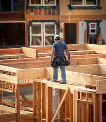 Above view of a construction worker walking on the edge of framing on the wall of a building under...