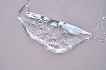 A drop of lubricant or cosmetic gel on a dusty pink background.