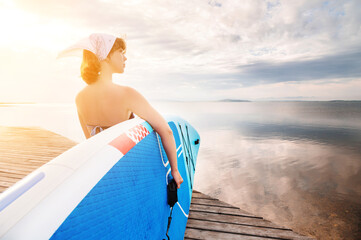Young beautiful woman in a bikini holds a SUP board on the sea beach. The girl carries a board...