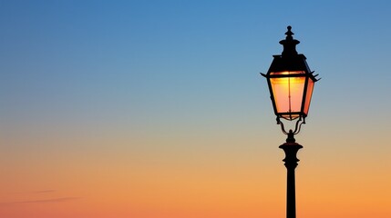 Obraz premium Victorian street lamp in silhouette against clear sky lit by sunset glow